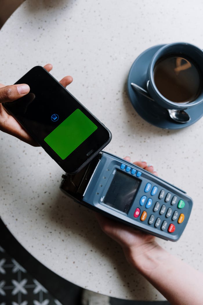 services-02 Smartphone making contactless payment on card reader next to coffee cup.