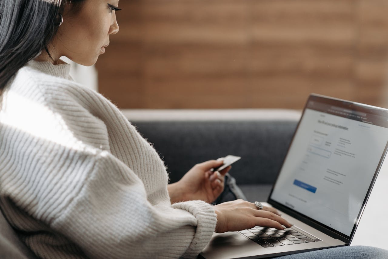 about-us Woman sitting on a couch, shopping online using a laptop and a credit card.