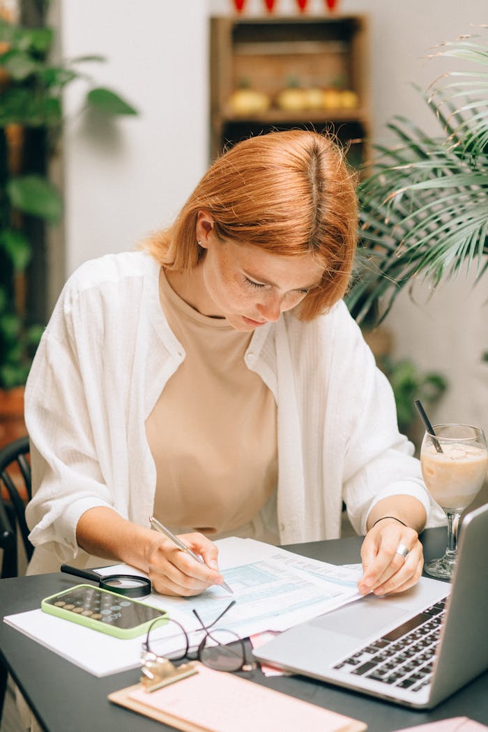 about-us Woman analyzing financial documents using laptop and calculator indoors.